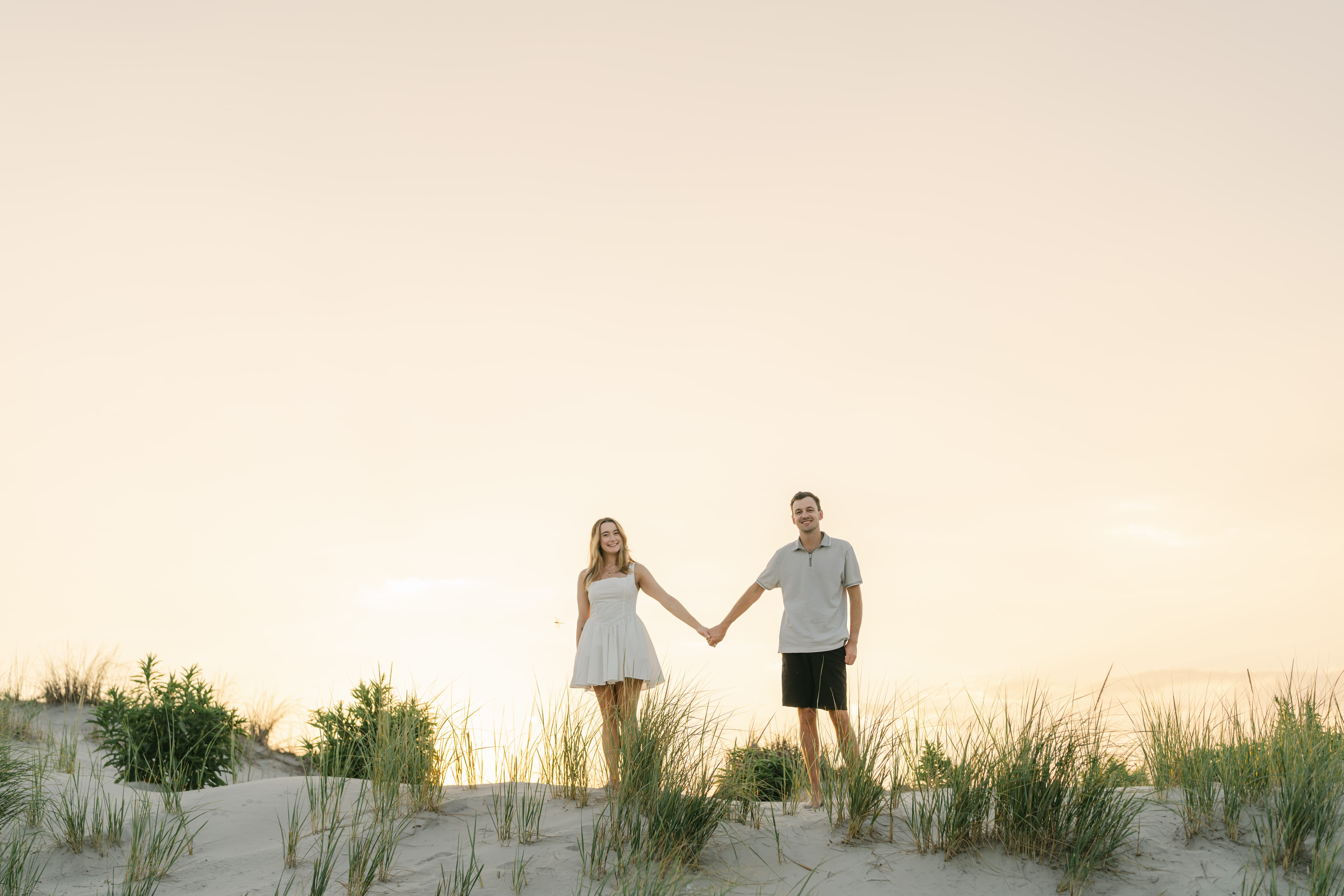 John and Samantha holding hands in the dune grass at sunrise